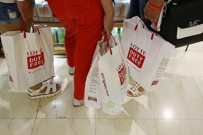 Customers (above) carrying Lotte Duty Free shopping bags in Seoul. The South Korean operator will take over the 18 liquor and tobacco concession stores managed by DFS (left) at Changi Airport next year.