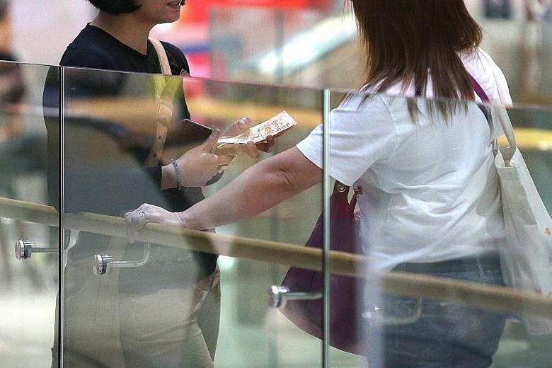 A go-between (right) with a maid after handing money over to her outside a telco shop at AMK Hub, with instructions on which mobile subscription plan to sign up for. ST PHOTO: SHINTARO TAY