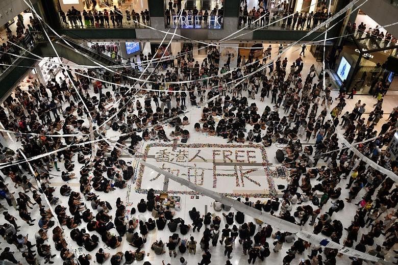 Above: Protesters folding paper cranes at a Sha Tin mall to form the words "Free HK" this month. The event was one of many community activities to maintain the momentum of the protest movement. Below: Hundreds gathering under a flyover in Kwun Tong o