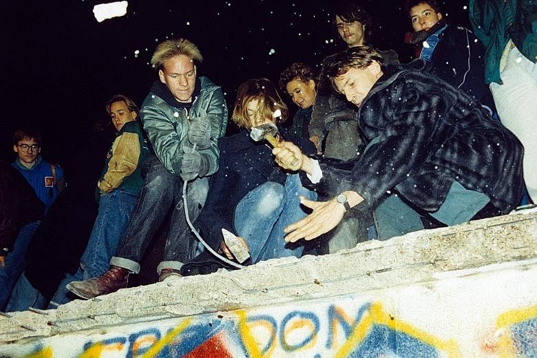 West Berliners (above) on Nov 10, 1989, hammering the graffiti-covered remains of the Berlin Wall. But the next day, East German border guards are seen fixing a section of the wall. The fall of the Berlin Wall ushered in the end of communism and Germany's