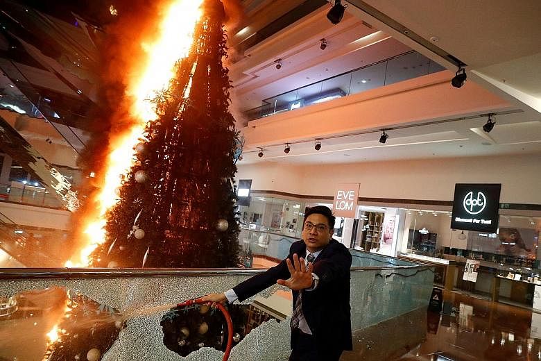 A man trying to extinguish a burning Christmas tree at Festival Walk mall in Kowloon Tong, Hong Kong, on Tuesday. The shopping centre, owned by Singapore-listed Mapletree North Asia Commercial Trust, suffered "extensive damage" caused by protesters o