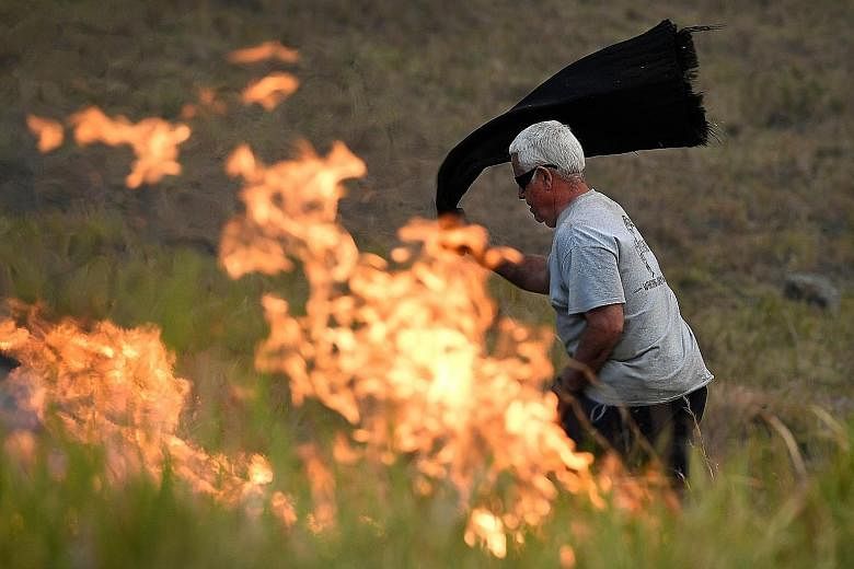A man using a wet towel to put out flames as they encroached on farmland near the town of Taree, some 350km north of Sydney, yesterday. The death toll from bush fires in eastern Australia has risen to four after a man's body was discovered in a scorc