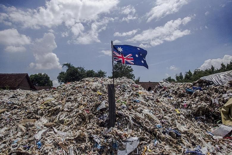 A port employee locking a container filled with waste set to be sent back to its origin country, Australia. An Australian flag protruding from a mound of plastic waste at an imported-plastic dump site in Mojokerto, East Java. The Indonesian authoriti