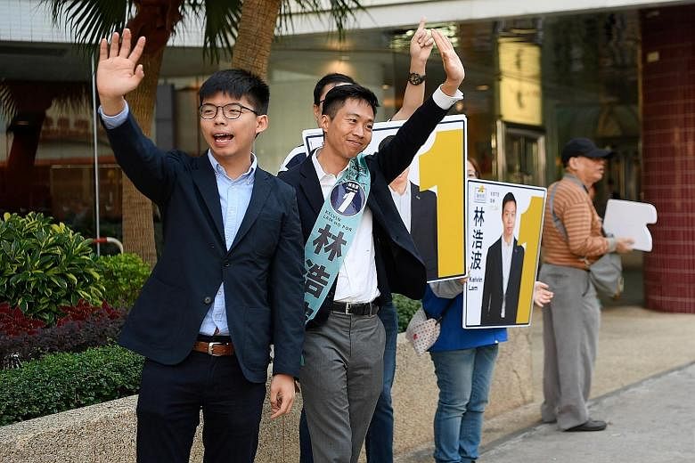 Above: Activist Joshua Wong (with glasses) campaigning for Mr Kelvin Lam, a candidate in the district council elections, in Hong Kong yesterday. Left: Staff getting a polling station ready for the polls, seen as a referendum on the months of protests