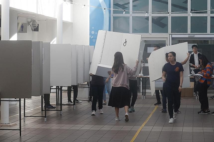 Above: Activist Joshua Wong (with glasses) campaigning for Mr Kelvin Lam, a candidate in the district council elections, in Hong Kong yesterday. Left: Staff getting a polling station ready for the polls, seen as a referendum on the months of protests