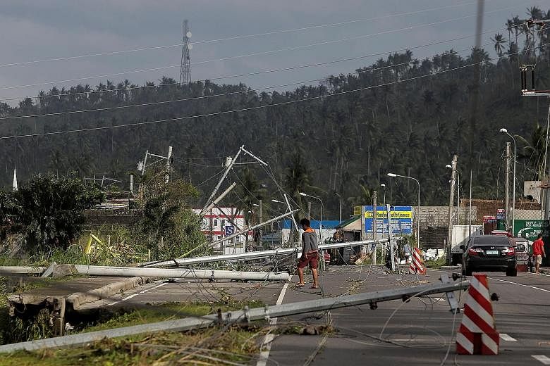 A man walking past fallen electric poles on the main highway after Typhoon Kammuri hit Camalig town in the Philippines yesterday. PHOTO: REUTERS Villagers working among damaged houses in the aftermath of Typhoon Kammuri in Legazpi city, the Philippin