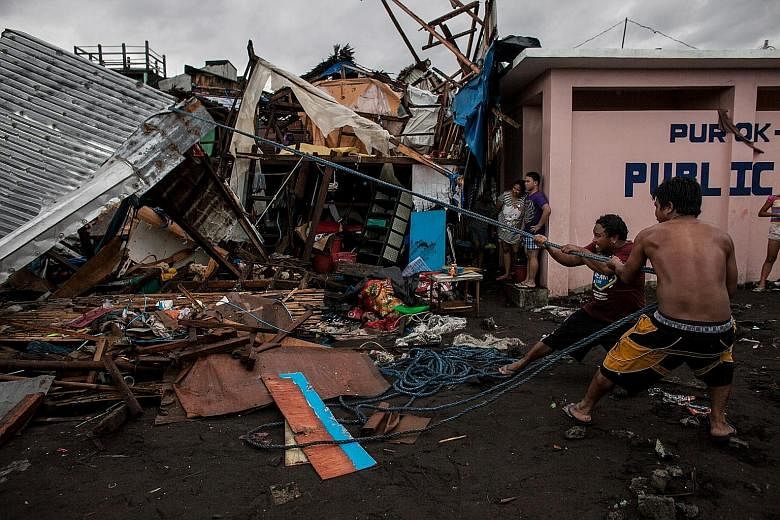 A man walking past fallen electric poles on the main highway after Typhoon Kammuri hit Camalig town in the Philippines yesterday. PHOTO: REUTERS Villagers working among damaged houses in the aftermath of Typhoon Kammuri in Legazpi city, the Philippin