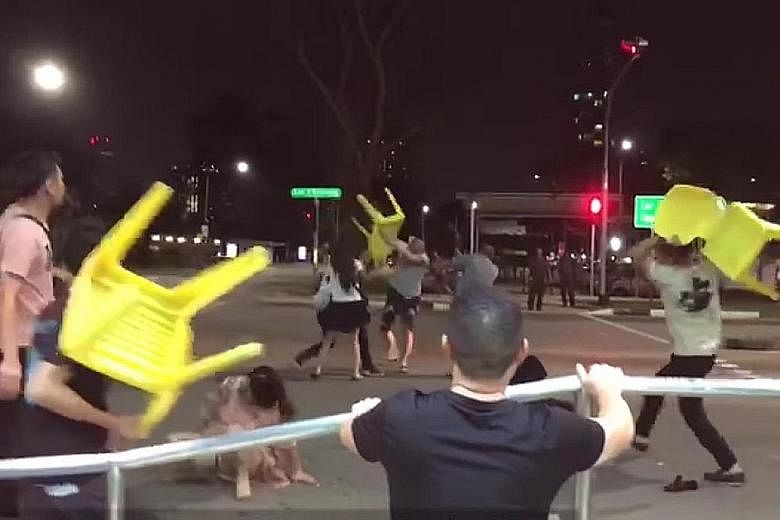 A screengrab of the video shared on Facebook by Sg Chinese Community showing some men involved in the brawl brandishing yellow chairs, with the woman in pink on the ground. PHOTO: SG CHINESE COMMUNITY/ FACEBOOK