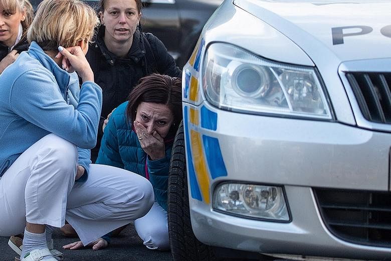 Staff of University Hospital in Ostrava, the Czech Republic, hiding behind a police vehicle yesterday, during a shooting spree by a gunman who later killed himself. PHOTO: EPA-EFE