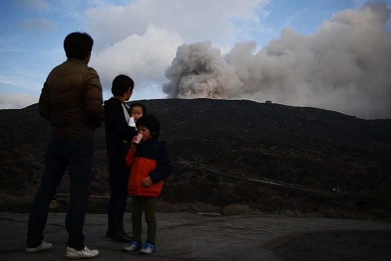 A family standing near Mount Aso, a large active volcano in Kumamoto prefecture, yesterday. The mountain's caldera has a circumference of more than 100km and is one of the largest in the world. It dominates the south-western main island of Kyushu, wh