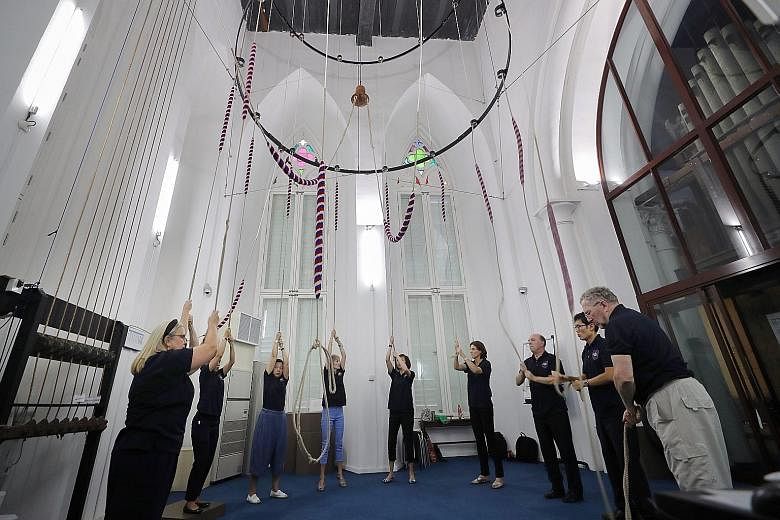 One of the team's trainers David Smith (at right) and tower captain Benjamin Tai (beside him) among bell ringers at St Andrew's Cathedral yanking on ropes attached to a custom-made structure that holds the bells, swinging them rhythmically through a 