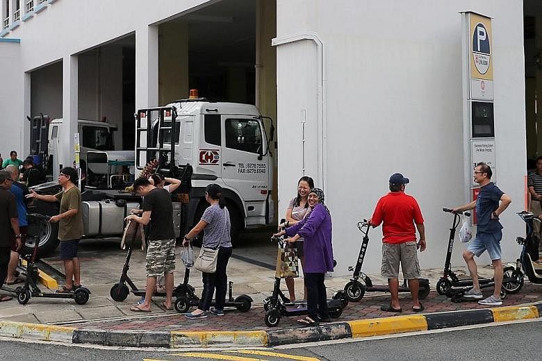 Mr Shawn Tan (front) and Mr Khairul dismantling e-scooters at their workstation in Virogreen's warehouse in Tuas. Each of them dismantles about 20 PMDs a day. The long queue at a designated e-scooter disposal point at a multi-storey carpark behind Na