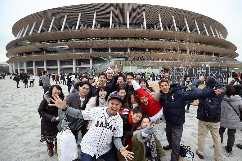 Visitors posing in front of Tokyo's new National Stadium, the main venue for next year's Olympic Games. But an estimated 3 billion yen is needed to move the marathon and walking races to Sapporo to avoid the worst of Tokyo's summer heat.