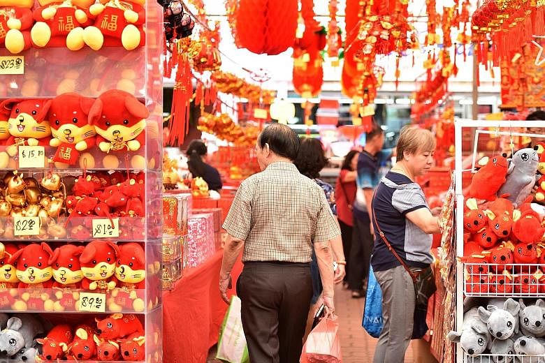 Shoppers browsing at a fair selling Chinese New Year decorations and mouse plush toys for the Year of the Rat in Ang Mo Kio on Tuesday. ST PHOTO: KELLY HUI A woman (above) posing for a photo with tangerines at a Chinese New Year goods stall and stude