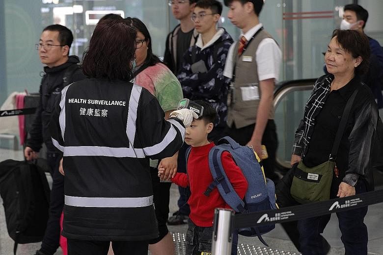 A health surveillance officer checking the temperature of passengers near the immigration counters at the Hong Kong International Airport on Saturday. The latest seven patients in Hong Kong are reported to be in stable condition and quarantined in di
