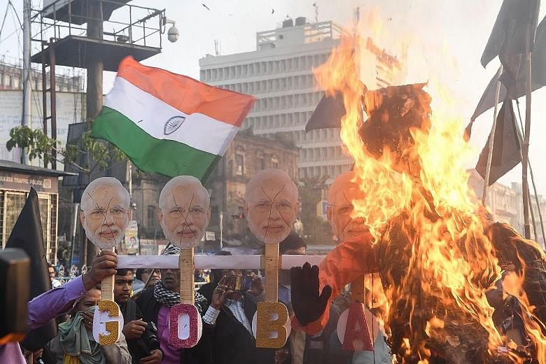 Activists (left) burning masks with the face of India's Prime Minister Narendra Modi, and others (below, left) displaying banners and shouting slogans against Mr Modi as they protested against India's new citizenship law in Kolkata yesterday.