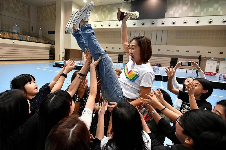 Louise Khng, 37, head coach of the national women's floorball team, being thrown in the air by her players while holding her appreciation trophy during Singapore Floorball Association's appreciation lunch at Our Tampines Hub yesterday. Khng took up t