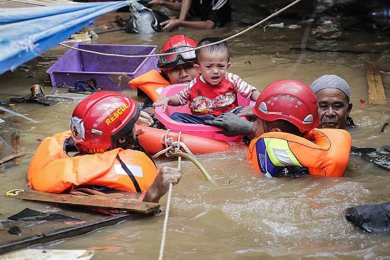 Above: Workers collecting rubbish during a clean-up after floods over the New Year in the Indonesian capital Jakarta. Below: Rescuers evacuating a boy from a flooded area in the capital on Jan 2. PHOTOS: ASSOCIATED PRESS, EPA-EFE