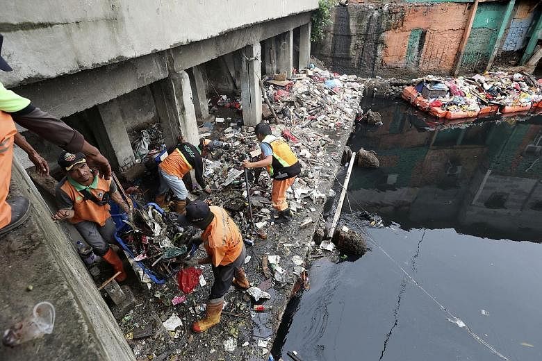 Above: Workers collecting rubbish during a clean-up after floods over the New Year in the Indonesian capital Jakarta. Below: Rescuers evacuating a boy from a flooded area in the capital on Jan 2. PHOTOS: ASSOCIATED PRESS, EPA-EFE