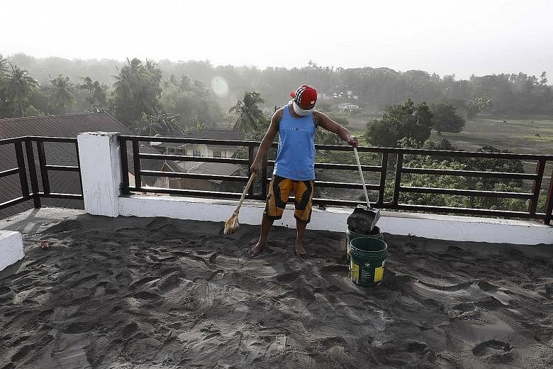A resident sweeping up ash that had accumulated on the roof of his home in Agoncillo town, in Batangas province, yesterday.