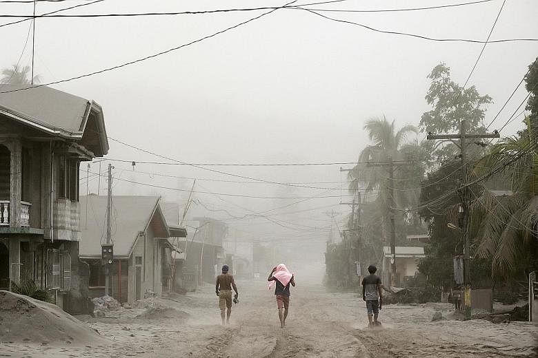 Residents living in Agoncillo, Batangas City, near the erupting Taal volcano, making their way through ash-covered streets yesterday.