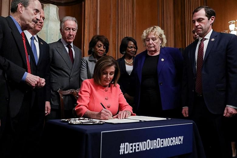 US House Speaker Nancy Pelosi signing the two articles impeaching President Donald Trump on Wednesday, with impeachment managers and committee chairs from the Democratic Party looking on. PHOTO: REUTERS
