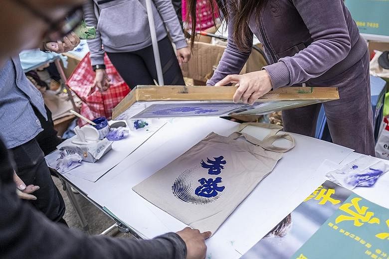 Protest banners can be seen at a Chinese New Year fair (above) in the Sai Ying Pun district. One stall (left) prints and gives away cloth bags with Chinese calligraphy ambigrams using characters for both "Hong Kong" and "add oil", a popular phrase of