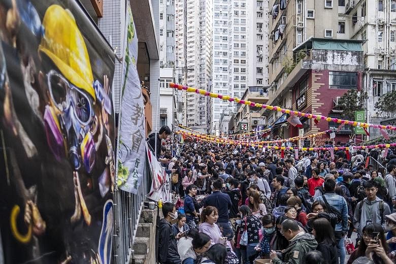 Protest banners can be seen at a Chinese New Year fair (above) in the Sai Ying Pun district. One stall (left) prints and gives away cloth bags with Chinese calligraphy ambigrams using characters for both "Hong Kong" and "add oil", a popular phrase of