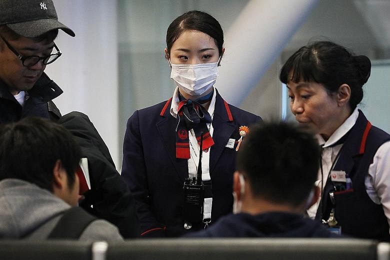 Above: A Japan Airlines employee wearing a face mask while at work at Los Angeles International Airport. The US State Department has warned travellers to exercise increased caution in China. Below: