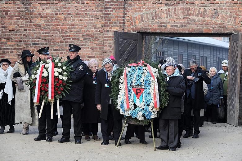 Above: An Auschwitz survivor dressed in a blue and white striped scarf symbolic of the uniforms prisoners wore. Right: Former prisoners at a wreath-laying ceremony in front of the Death Wall in Oswiecim, Poland, yesterday. PHOTOS: REUTERS, EPA-EFE