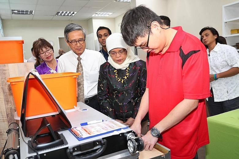 President Halimah Yacob, Autism Association chairman Ho Swee Huat and Autism Resource Centre president Denise Phua, who is also an MP for Jalan Besar GRC, observing Mr Davin Yeap operate a laser cutting machine at the Eden Centre for Adults in Clemen