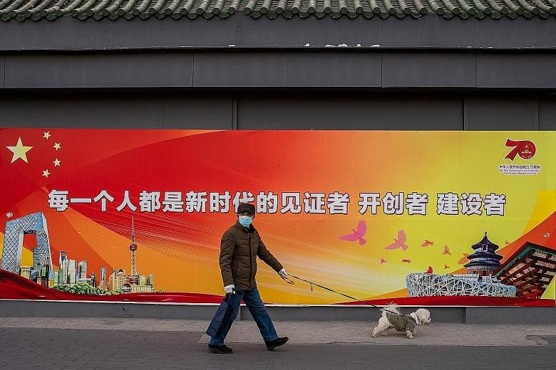 A man wearing two protective masks and gloves walking his dog last Friday past a government propaganda poster in Beijing that reads "Everyone is a witness of the new era".