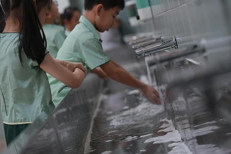 Above: Farrer Park Primary School pupils taking turns to wash their hands before going for recess yesterday morning. Left: Primary 2 pupils at Farrer Park Primary School recording their temperatures in their books after a temperature-taking exercise 