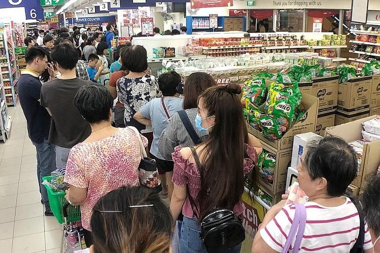 Shoppers queueing to pay for essential items at the FairPrice supermarket at HDB Hub in Toa Payoh yesterday. Items began flying off the shelves at some supermarkets here after Singapore announced earlier in the day that it would be raising its diseas