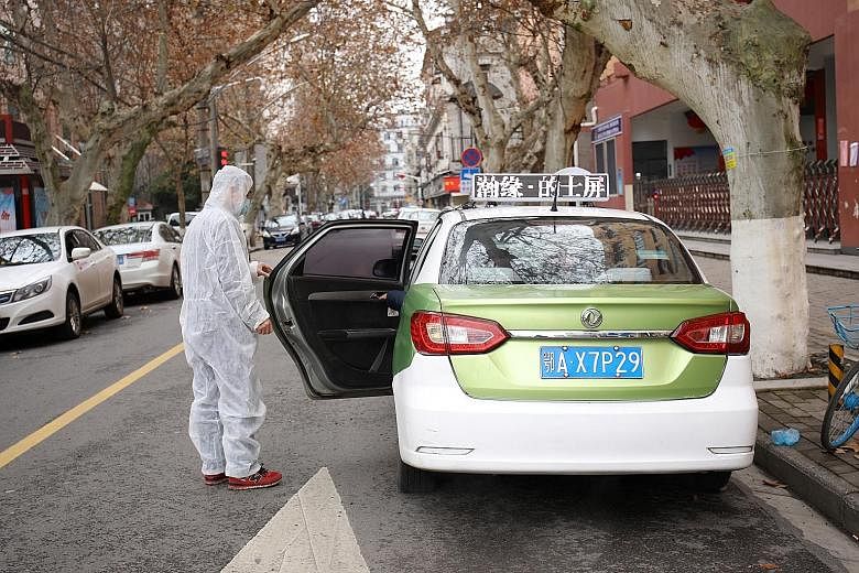 A man in a protective suit holding the door for a cab passenger in Wuhan. Vice-Premier Sun Chunlan said during a visit to Wuhan on Thursday that the city and country face "wartime conditions". A blocked road in Wuhan, following an outbreak of the cor