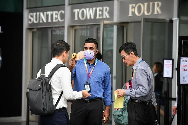 An employee getting his temperature checked before entering Suntec City yesterday. Some firms have also cancelled large-scale internal meetings such as training sessions, seminars and workshops. ST PHOTO: CHONG JUN LIANG
