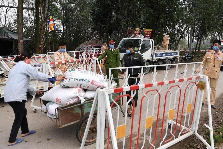 Police allowing a resident with goods to pass through a checkpoint yesterday at one of the six villages that make up Son Loi, about 40km from Hanoi. The farming region will be locked down for 20 days.