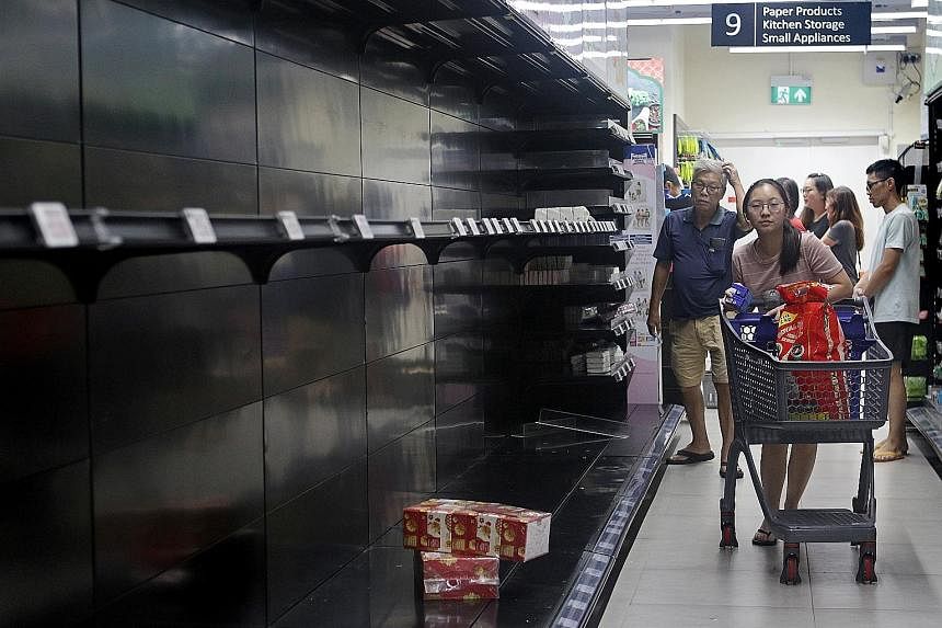 Scenes of panic buying were seen at supermarkets across the island last weekend. A shopper at a FairPrice Finest outlet in Paya Lebar (above) walking past empty shelves last Saturday.