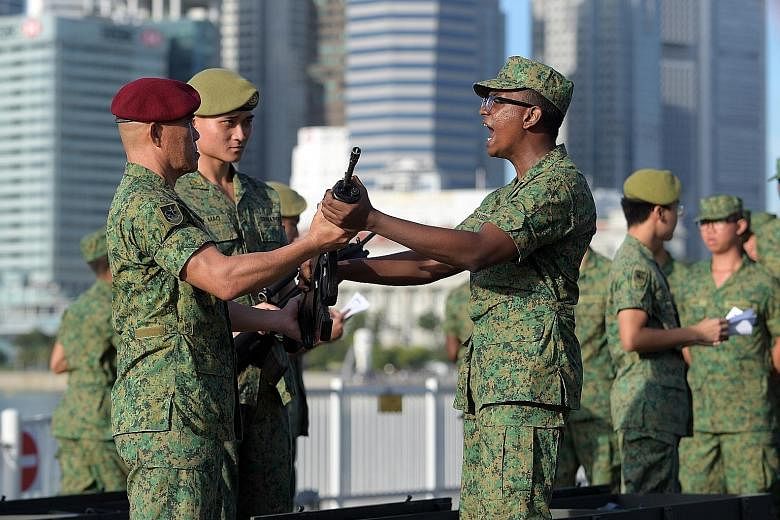 Basic Military Training Centre recruits receiving their SAR-21 rifles from their officers during the Total Defence Day Commemoration Event yesterday at The Float @ Marina Bay.