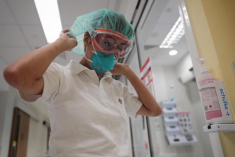 Nurse clinician Priscilla Fu going through the first steps in the process of donning personal protective equipment - putting on an N95 mask, goggles and shower cap. She has to "gown up" in this way when she enters an isolation room in which a coronav