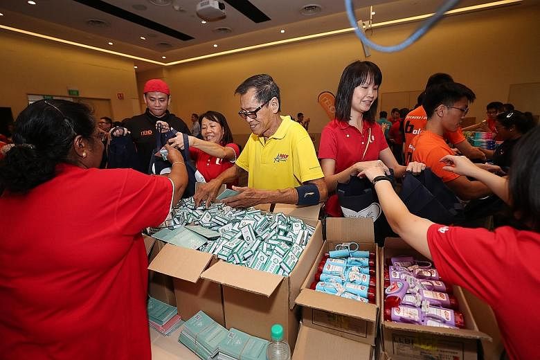 Volunteers preparing the care packs by adding items from various stations. Each pack contains items such as snacks, hand sanitisers and personal hygiene products.