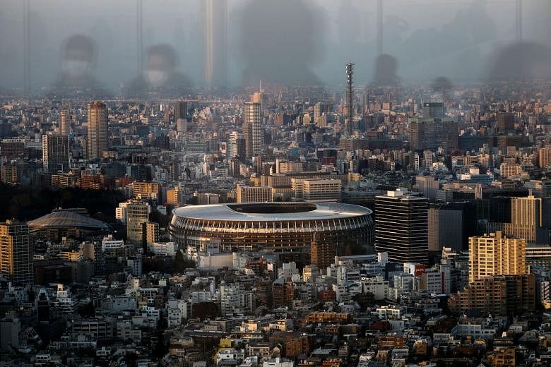 A view of Tokyo's new National Stadium for the July 24-Aug 9 Olympic Games, as people wearing masks to protect themselves from the coronavirus are reflected at the Shibuya Sky observation deck.