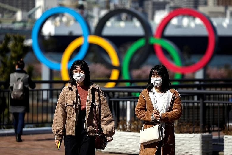 People wearing protective face masks, following an outbreak of the coronavirus, in front of the giant Olympic rings at the waterfront area at Odaiba Marine Park in Tokyo. 