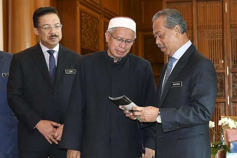 Malaysia's newly appointed Prime Minister Muhyiddin Yassin (right) looking at a book given to him by Federal Territory Mufti Zulkifli Mohamad Al-Bakri at Bangunan Perdana Putra in Putrajaya yesterday, as Chief Secretary to the Government Mohd Zuki Al