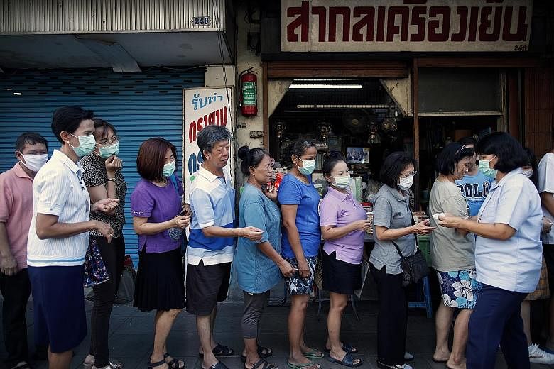 An official distributing queue tickets to people waiting to buy face masks outside a Bangkok pharmacy yesterday. Public Health Minister Anutin Charnvirakul had earlier declared that people coming from 11 virus-hit areas would need to quarantine thems