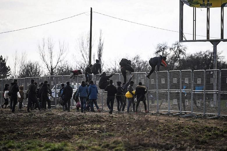 Migrants scaling a fence at Turkey's border with Greece on Wednesday. Thousands have made for Greece since Ankara said on Feb 28 that it would let migrants cross its borders into Europe, reneging on a 2016 deal in which Brussels agreed to pay billion
