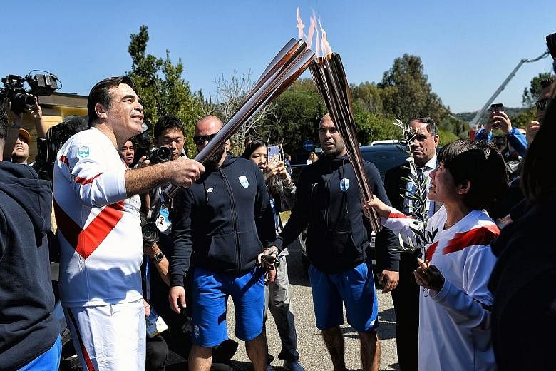 Japan's 2004 Olympic marathon champion Mizuki Noguchi, the second torch bearer, passing the 2020 Tokyo Olympic torch to Margaritis Schinas, the European Commission vice president on Thursday. They are in front of the Temple of Hera in Ancient Olympia
