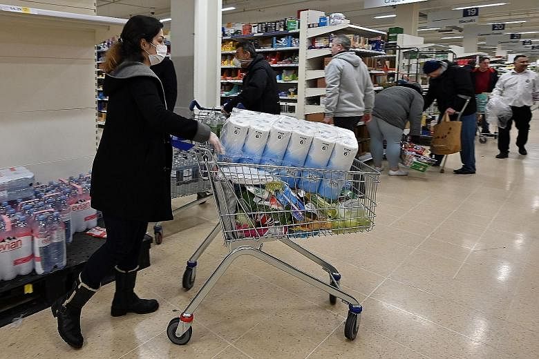 A woman wearing a face mask carting away toilet paper at a supermarket in London last Saturday. Consumers, worried about shortages during the pandemic, have started stockpiling household products.