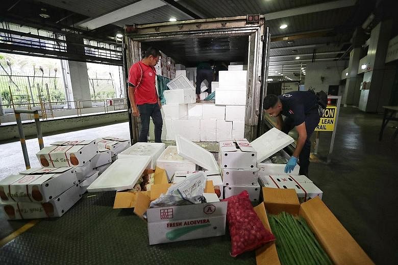 A truck driver from Malaysia having his temperature taken at the Woodlands Checkpoint yesterday. Most wholesalers and retailers here received their goods from Malaysia as usual yesterday. Immigration and Checkpoints Authority officers inspecting item