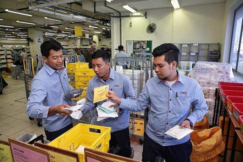 SingPost employees (from left) Hairul Azhar Ismail, 29, Mohammad Hussin Supardi, 30, and Mohd Syafiq Mohd Yusoff, 24, sorting mail for delivery at the Kallang Delivery Base yesterday. They are among about 400 Malaysian SingPost staff who are staying 